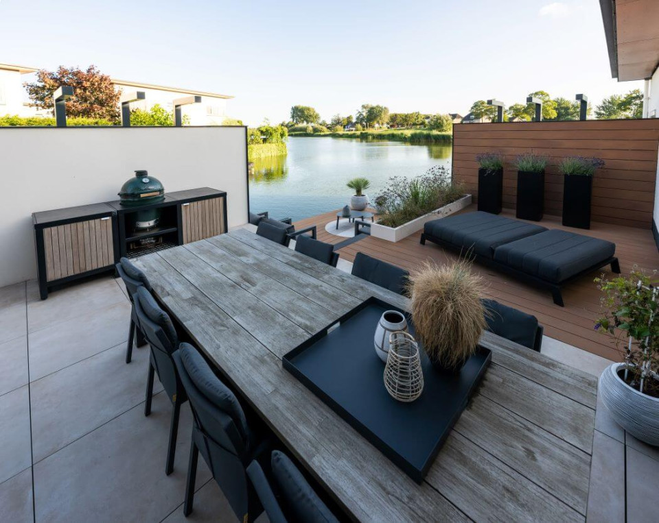 Buitenkeuken van Cooxs bij een tuin aan het water, met een avondterras en dinertafel voor een gezellige sfeer.