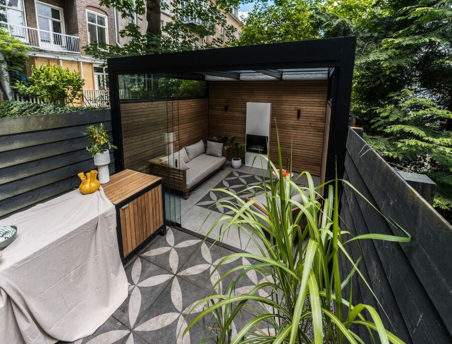 Eigentijds tuin ontwerp bijgebouw openhaard knusse lounge set grote tegels planten potten siergrassen buitenkeuken top10 (1)