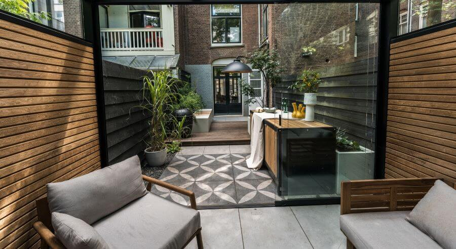 Eigentijds tuin ontwerp overkapping lounge set buitenkeuken barbecue verlichting siergrassen grote tegels houten vloer sfeer idee (1)