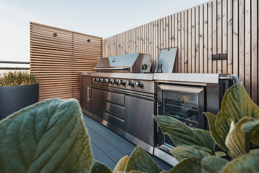 Modern dakterras ontwerp buitenkeuken barbecue houten vloer planten potten siergrassen houten wand verlichting sfeer idee (1)