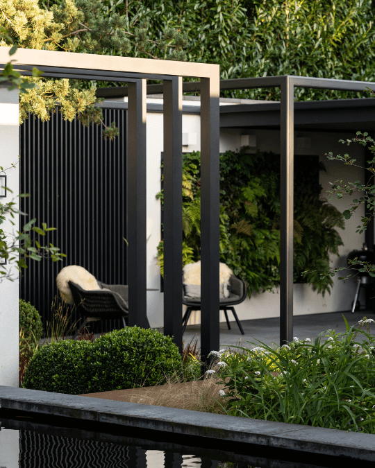 Strakke, zwarte industri&euml;le pergola als statement in een moderne tuin, met een minimalistische en luxe uitstraling.